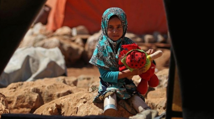 A young refugee girl missing her legs sits on the ground