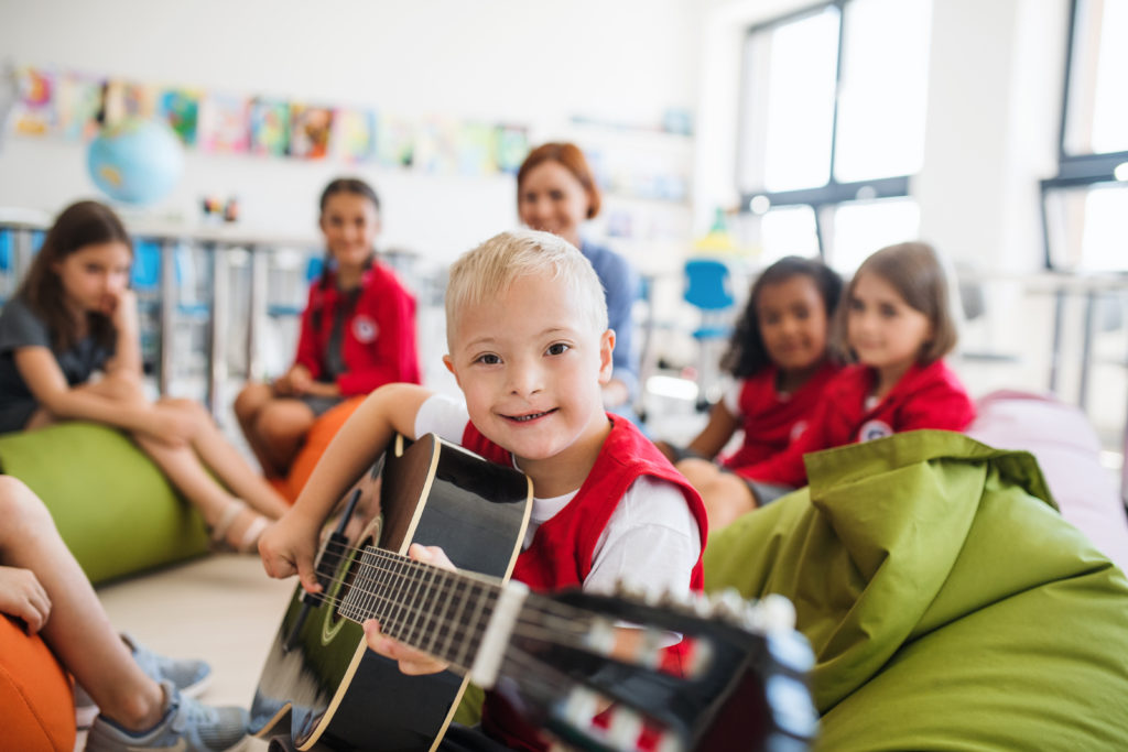 A boy with down syndrome plays guitar surrounded by children